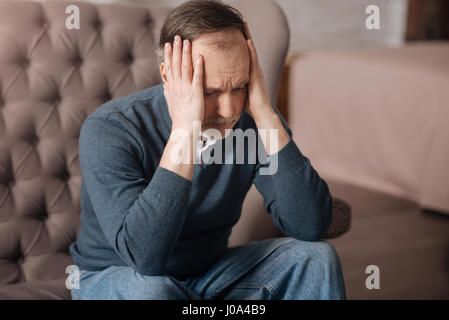 Alles ist verloren. Deprimiert Greis auf Couch sitzen und seine Schläfen mit Händen zu berühren. Stockfoto