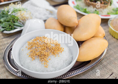 Enger Fokus auf klebrigen Reis von gerösteten Sojabohnen in weiße Schüssel mit gelbe Mango auf Platte abgedeckt. Stockfoto