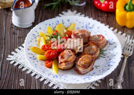 Schweinefilet in Speck und Bratkartoffeln, frischem Gemüse und Kräutern auf einem Holztisch im rustikalen Stil gebacken. Stockfoto