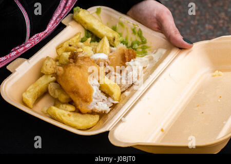 Eine Person hält und Essen Fisch und Chips aus einem Take-away Fach direkt am Meer in Llandudno, Nordwales Stockfoto