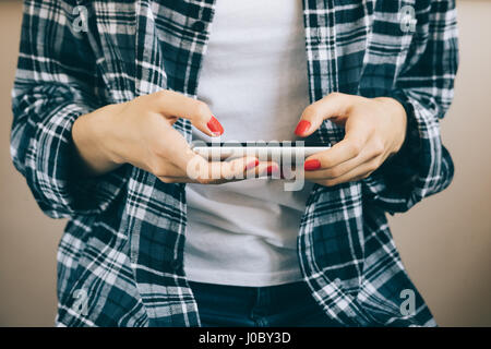 Zugeschnittenes Bild der Frau im karierten Hemd mit roten Maniküre hält Smartphone in den Händen, Nahaufnahme Stockfoto