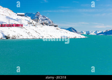 Bernina Express Zug im verschneiten Tal umgeben von See Bianco, Berninapass, Kanton Graubünden, Engadin, Schweiz Stockfoto