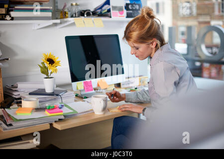 Frau sitzt am Schreibtisch im Büro auf Merkzettel schreiben Stockfoto