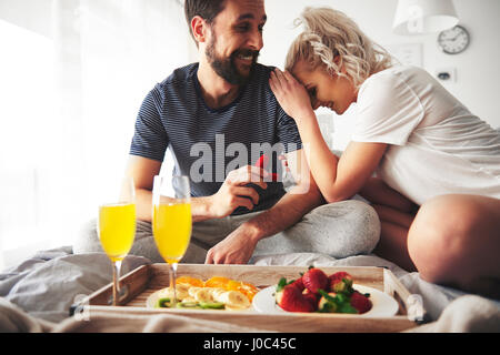 Paar sitzt am Bett, Mann schlägt vor, halten offene Ring-box Stockfoto