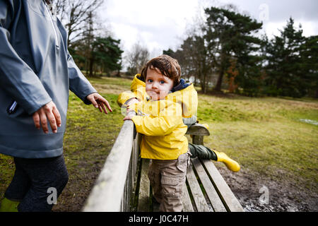 Baby Junge mit Mutter im gelben Anorak auf Parkbank Stockfoto