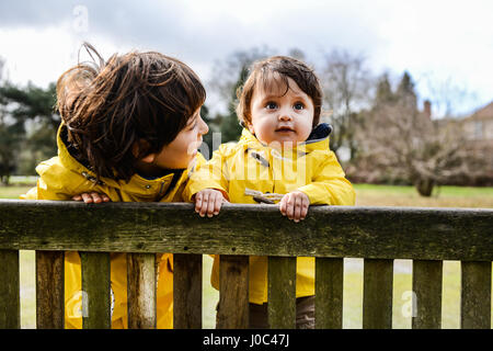 Porträt des jungen und Big Brother im gelben Anoraks auf Parkbank Stockfoto