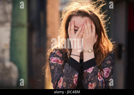 Porträt der jungen Frau bedeckte Gesicht mit den Händen, Bristol, UK Stockfoto