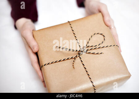 Frau mit Geschenk verpackt in Packpapier, dekoriert mit einer Schnur, Nahaufnahme Stockfoto