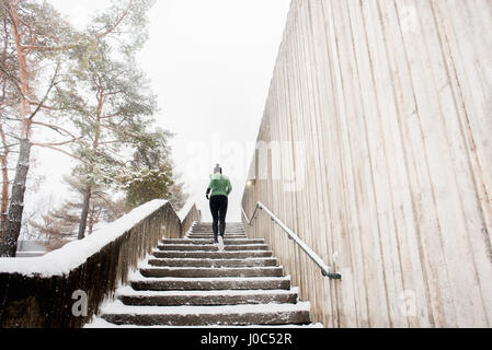 Rückansicht des jungen weiblichen Läufer in Strick Hut angerannt Schnee bedeckt Treppe Stockfoto