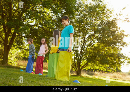 Mädchen und Jungen auf die Startlinie für Sackhüpfen im park Stockfoto
