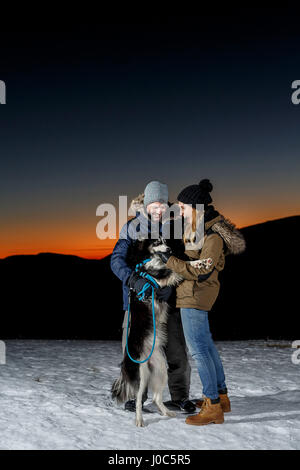 Paar mit Hund im Schnee in der Nacht spielen Stockfoto