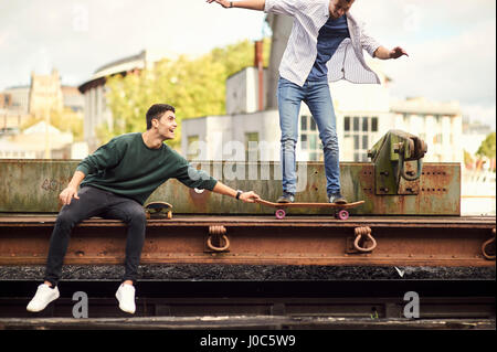 Zwei junge Männer, die mit dem Zug herumalbern verfolgen, balancieren auf Skateboard Bristol, UK Stockfoto