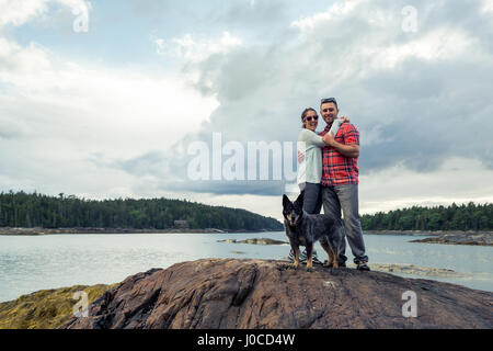 Porträt des romantischen Mitte Erwachsenen paar und Hund auf Felsen an der Küste von Maine, USA Stockfoto