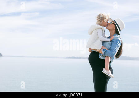 Schwangere Mutter Tochter an Küste küssen Stockfoto