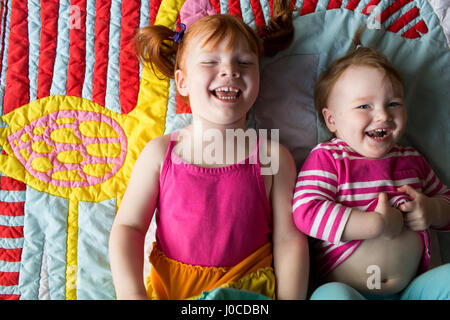 Porträt von zwei jungen Schwestern auf der Decke liegen, lachen Stockfoto