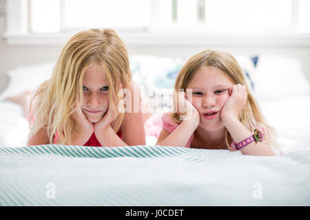 Porträt von Mädchen und Schwester Grimassen auf Bett Stockfoto