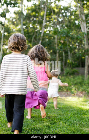 Rückansicht des weiblichen Kleinkind gefolgt von jungen und Mädchen im Garten Stockfoto