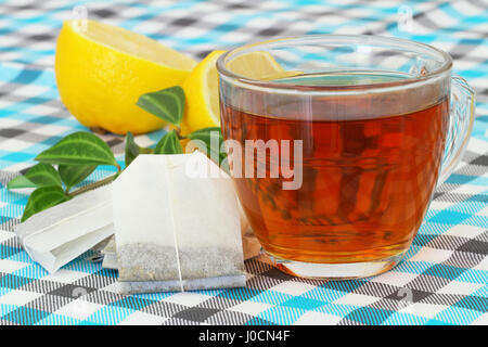 Tasse Tee, Teebeutel und frische Zitrone auf kariertem Stoff Stockfoto