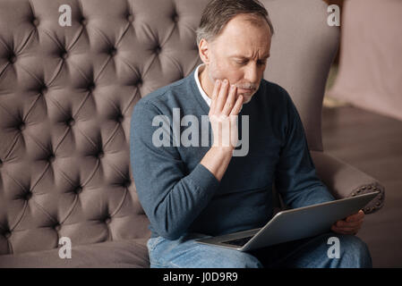 So verletzend. Porträt von senior gut aussehender Mann mit starken Zahnschmerzen auf Couch sitzen und Laptop zu Hause verwenden. Stockfoto