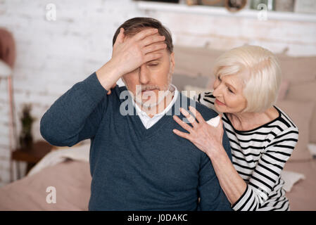 Ich bin krank. Ältere Mann schlecht fühlen und seine Stirn zu berühren, während seine Frau versucht, ihn zu unterstützen. Stockfoto