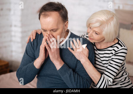 Allergie leidet. Ältere Frau Unterstützung älterer Ehemann bedeckte sein Gesicht beim Niesen. Stockfoto