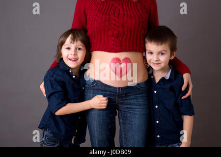 Schöne Kinder im Vorschulalter, Brüder, umarmt ihre schwangere Mutter, freudig erwartet großen Brüder zu sein. Rote Heide auf Mütter Bauch gezogen, küssen Stockfoto