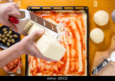 Mann reiben Käse auf einem Pizzateig. Pizza backen Stockfoto