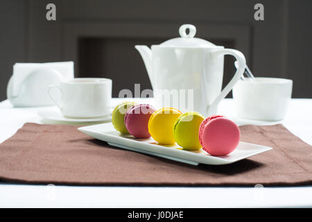 Bunte Makronen auf ein weißes Quadrat Platte süßen Macarons und Blumen. Vor dem Hintergrund der ein Tee-Set weiß Stockfoto