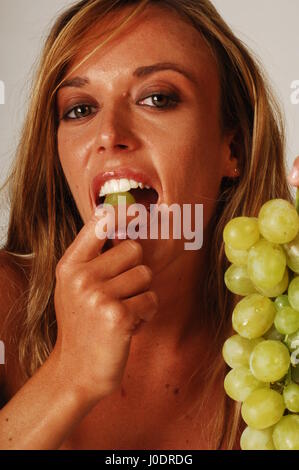 Eine blonde Frau essen eine Reihe von weißen Trauben, die auf einem weißen Hintergrund isoliert Stockfoto