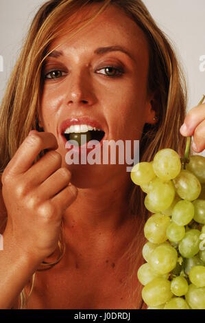 Eine blonde Frau essen eine Reihe von weißen Trauben, die auf einem weißen Hintergrund isoliert Stockfoto