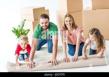 Glückliche junge Familie von vier abrollen Teppich nach dem Umzug in neues Haus Stockfoto