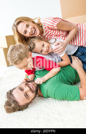 Glückliche junge vierköpfige Familie, die Spaß am Teppich liegen und lachen Stockfoto