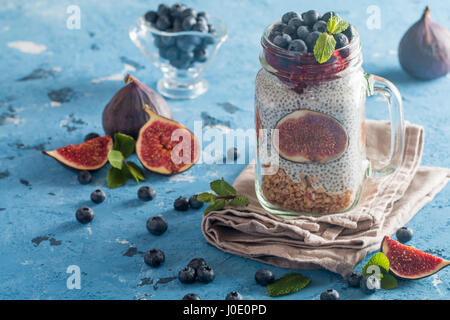 Glas von gesunden Frühstück mit Müsli, Pudding mit frischen Feigen, Chia-Samen und Beeren auf blauem Hintergrund Stockfoto