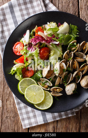 Feinkost-Venusmuscheln mit Kalk und Salat aus frischem Gemüse Nahaufnahme auf einer Platte. Vertikale Ansicht von oben Stockfoto