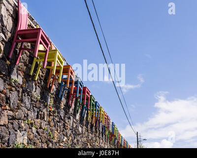 Bunte Stühle auf einer Steinmauer. Eine lange Reihe von Holzstühlen, malte helle Grundfarben Kanten einer groben Steinmauer in Sao Roque in der Nähe der Hauptstadt. Stockfoto