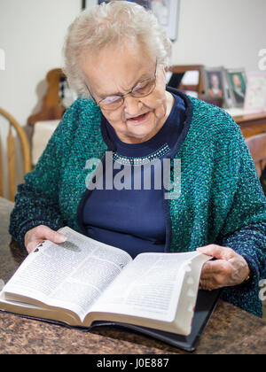 Eine Frau, eine Bibel zu lesen. Eine ältere Senioren liest und blättert in einer großen gedruckten Bibel. Stockfoto