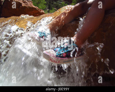 Ein Kind sitzt in einem kleinen Bach und genießt das Wasser spritzt über ihre Füße. Stockfoto