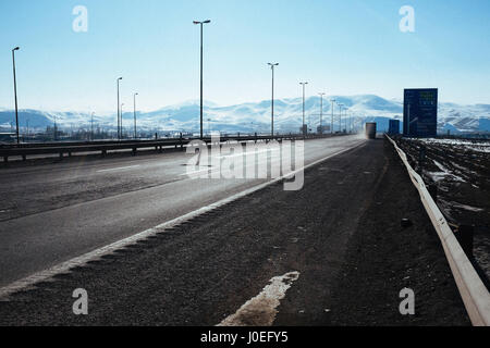 Lastwagen fahren durch die beeindruckende Landschaft mit Bergen, blauem Himmel und weißen Wolken auf der Fahrbahn zwischen Teheran und Tabriz im Iran. Stockfoto