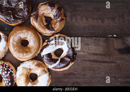 Hintergrund der Schokolade, Carmel, glasiert und Donuts über einen rustikalen Hintergrund mit textfreiraum gefüllt. Bild von oben. Stockfoto