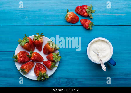 Flatlays. Draufsicht der frische, rote Erdbeeren auf einer Holzfläche und Sahne im Becher Stockfoto
