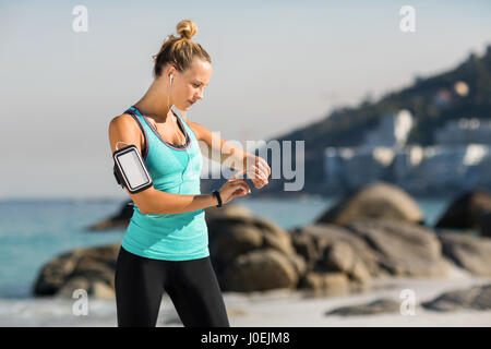 Junge Frau mit Smartphone auf Armbinde Musik hören am Strand Stockfoto