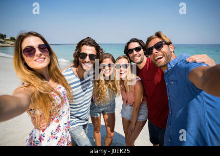 Fröhliche Freunde stehen an der Küste am Strand im sonnigen Tag Stockfoto