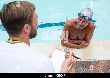 Schwimmen Sie Trainer, die Interaktion mit älteren Mann am Pool Stockfoto