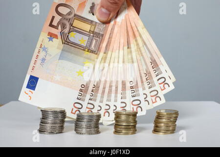 Hand, die Banknoten von 50 Euro und Euro-Münzen stapeln. Stockfoto
