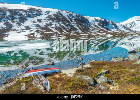 Alte Boote liegen an einem Seeufer, mit Eis & schneebedeckten Berge im Hintergrund - Norwegen rosten Stockfoto