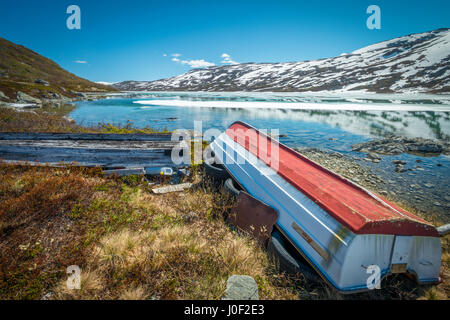 Alte Boote liegen verlassene am Rande ein Bergsee bis in den verschneiten Bergen Stockfoto