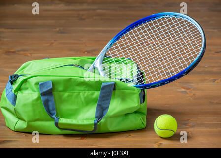 Ein Tennisschläger ragt aus einer grünen Sporttasche, Objekte auf dem Boden Stockfoto