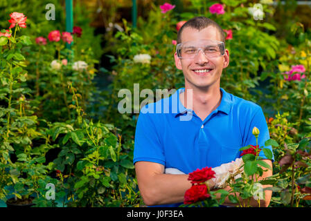 Glücklicher Mann mit Brille und Labor Handschuhe in einem Gewächshaus unter Blumen Stockfoto