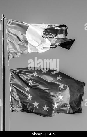 Allgemeine drei Farben Flagge und Europa Fahnenschwingen zusammen in isolierten grauen Himmelshintergrund. Schwarz und weiß. Konzept für alte finanzielle behandelt, uni Stockfoto