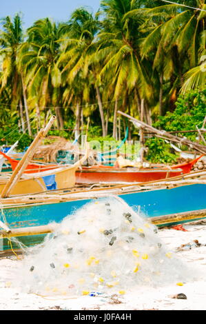 Fischernetz auf Korallen Sandstrand mit bunten Booten und Palmen im Hintergrund weiß Stockfoto